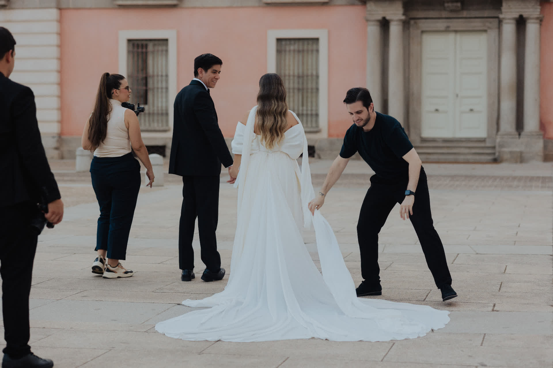 Nelson ajusta el vestido de la novia mientras camina de la mano del novio por una plaza histórica
