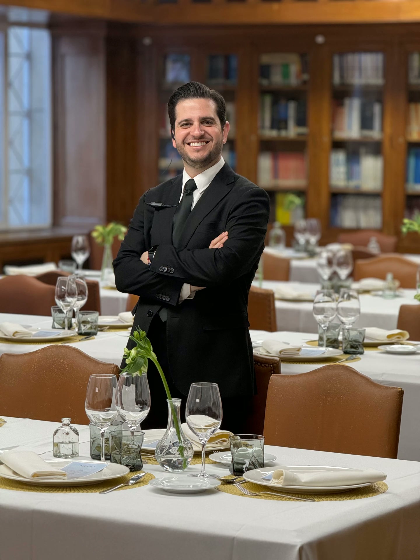 Nelson coordinando el servicio en un comedor elegante, entre copas y menús dispuestos en las mesas