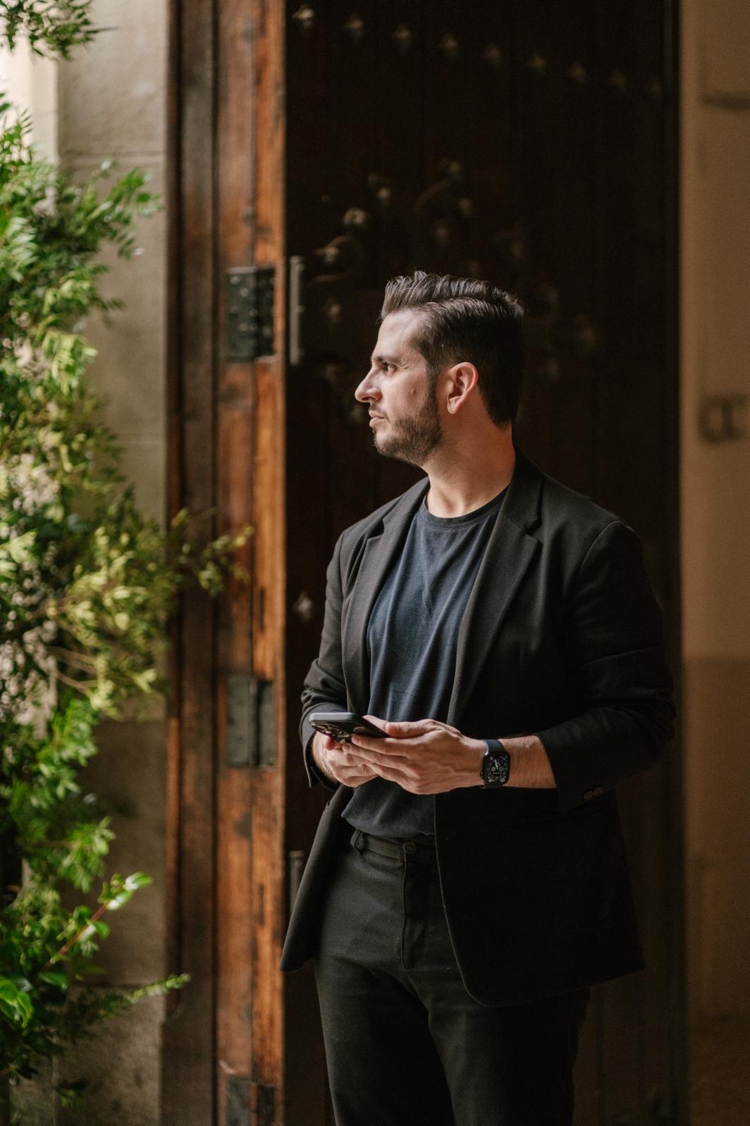 Nelson coordinando la llegada de invitados ante una puerta de madera rodeada de vegetación