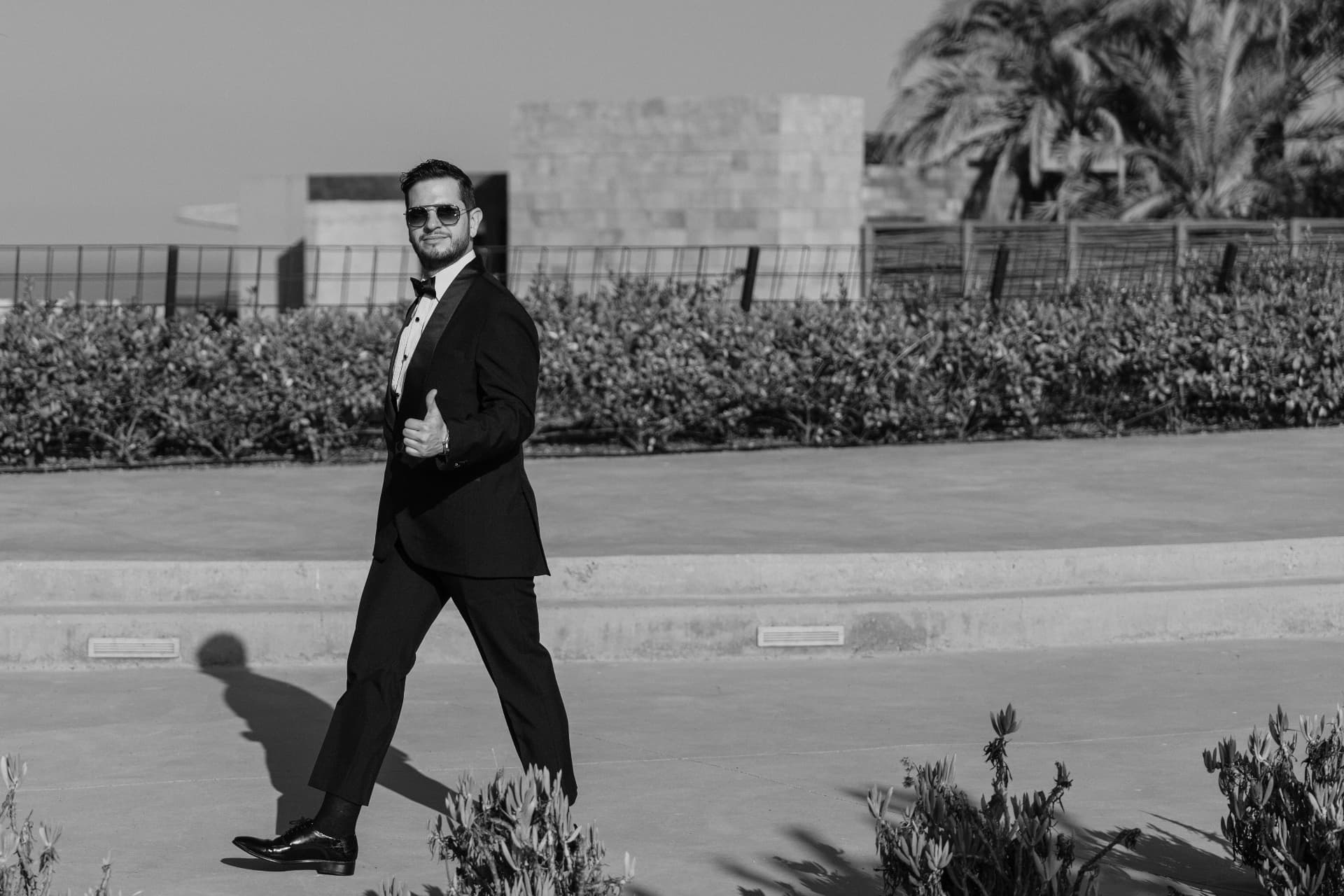 Novio de esmoquin sonriendo en una terraza al sol, en blanco y negro