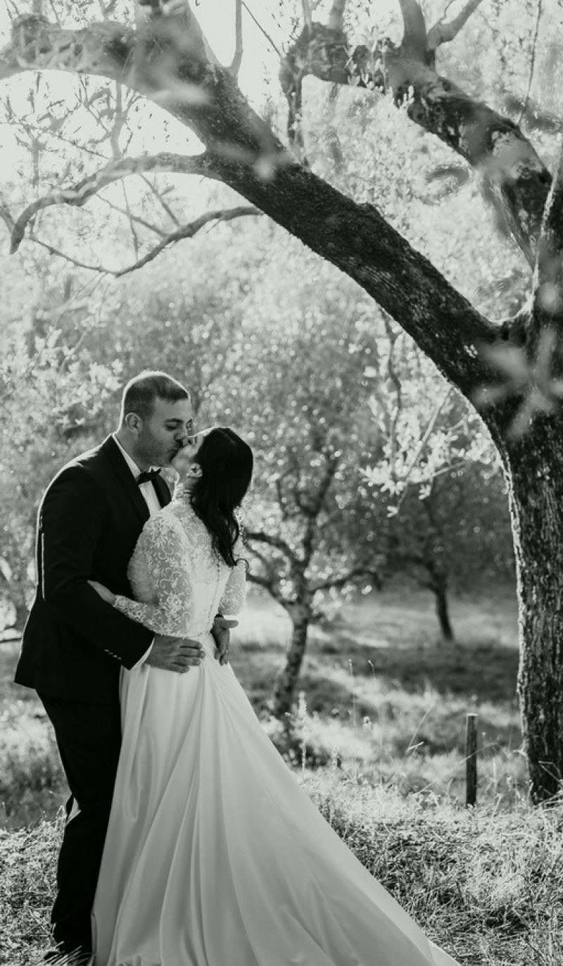 Novios besándose bajo un gran olivo, en blanco y negro