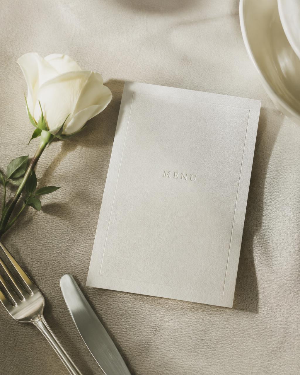 Menú de papel de algodón junto a una rosa blanca